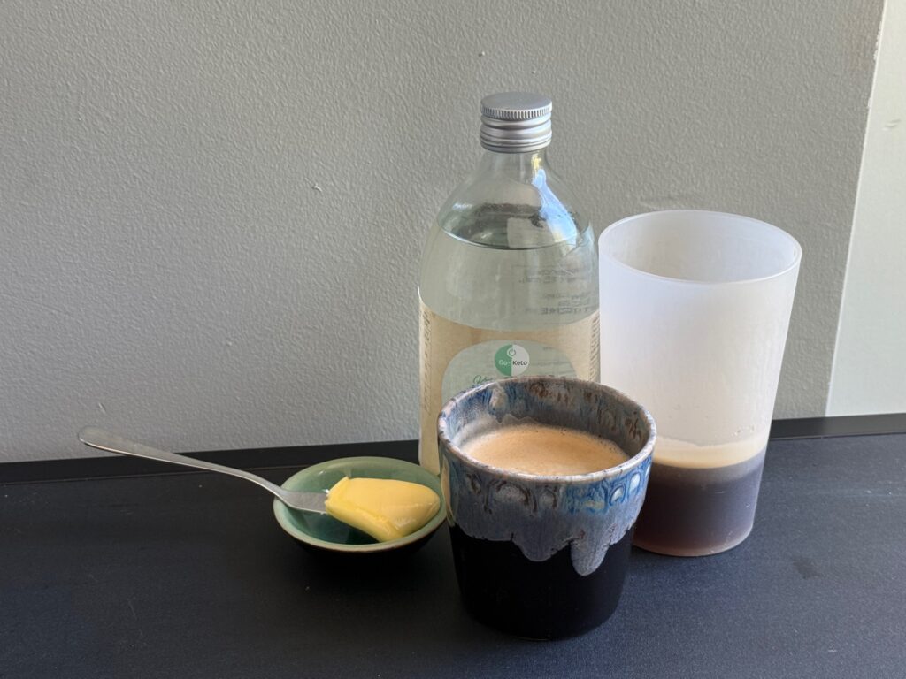 a cup of coffee and a spoon with butter and a bottle of liquid
